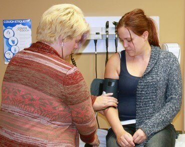 A photo of a female doctor checking the pulse of a female patient with a stethoscope and arm cuff.