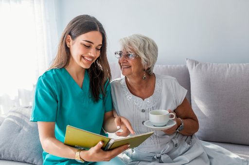 A photo of a young woman nurse reading off a notebook to an older woman patient.