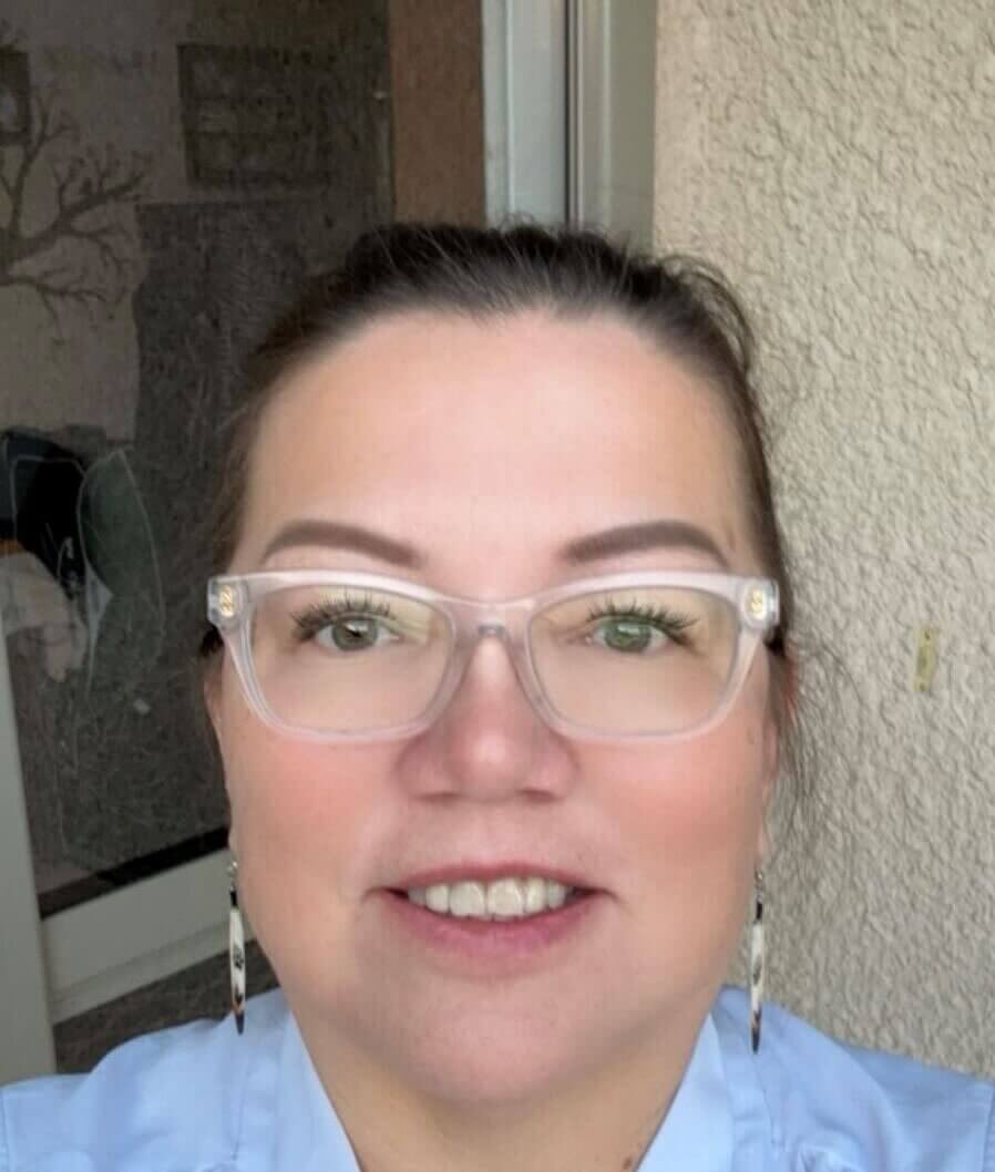 photo of Denise bear smiling in Glasses, earrings and light blue shirt.