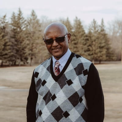 Male doctor with sunglasses outside with checked sweater over dress shirt and red tie.