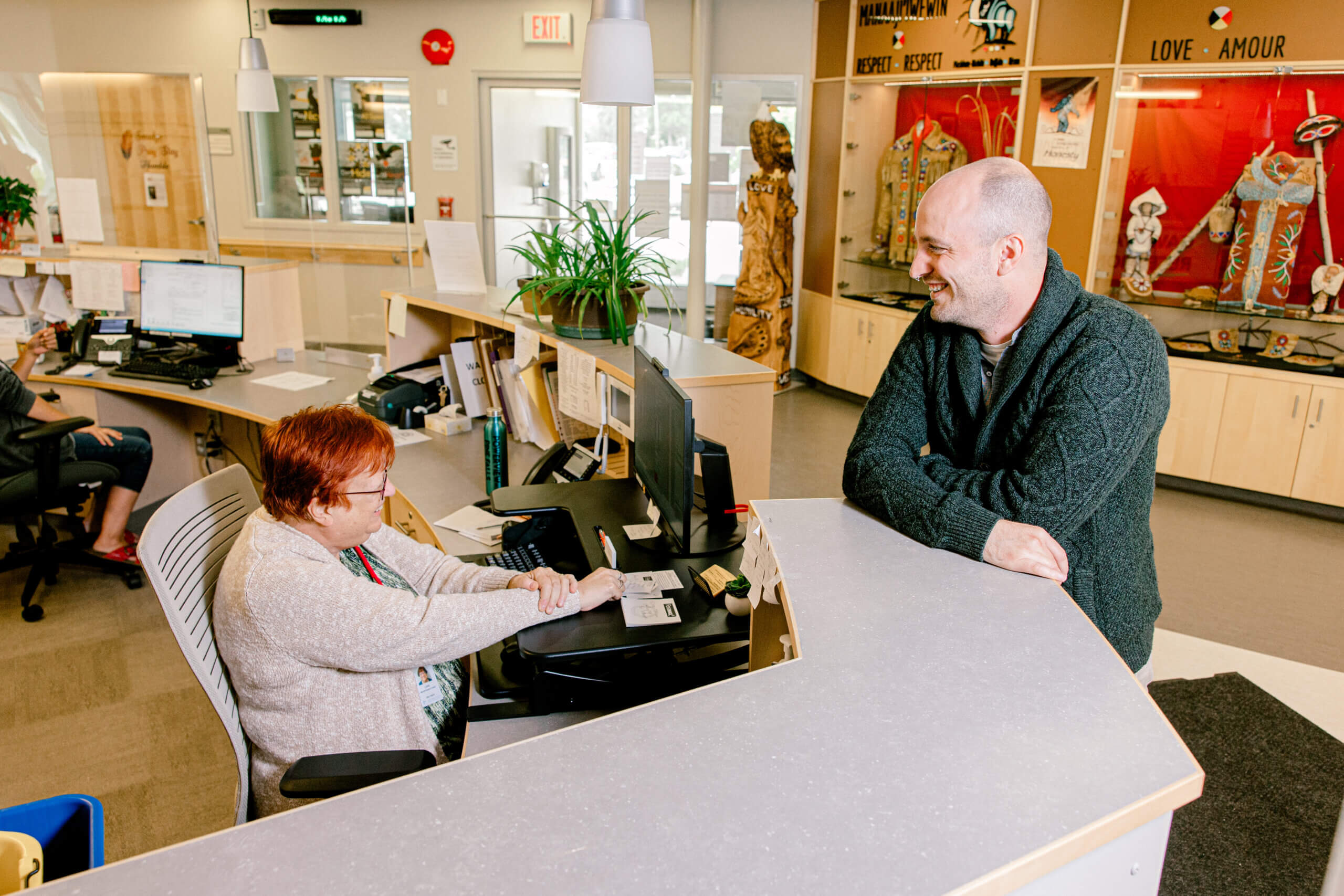 A photo of a female receptionist speaking to a male at the front desk.