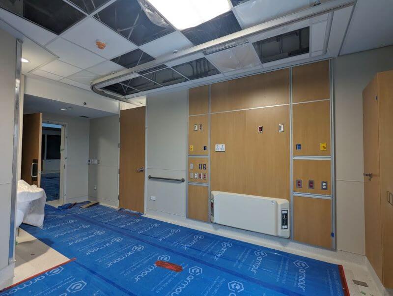 Blue covering on floor in patient room with millwork completed and the head wall attachments for the bed.