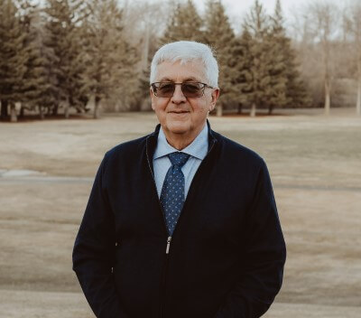 Male doctor with dark sunglasses, blue tie and blue shirt with black sweater.