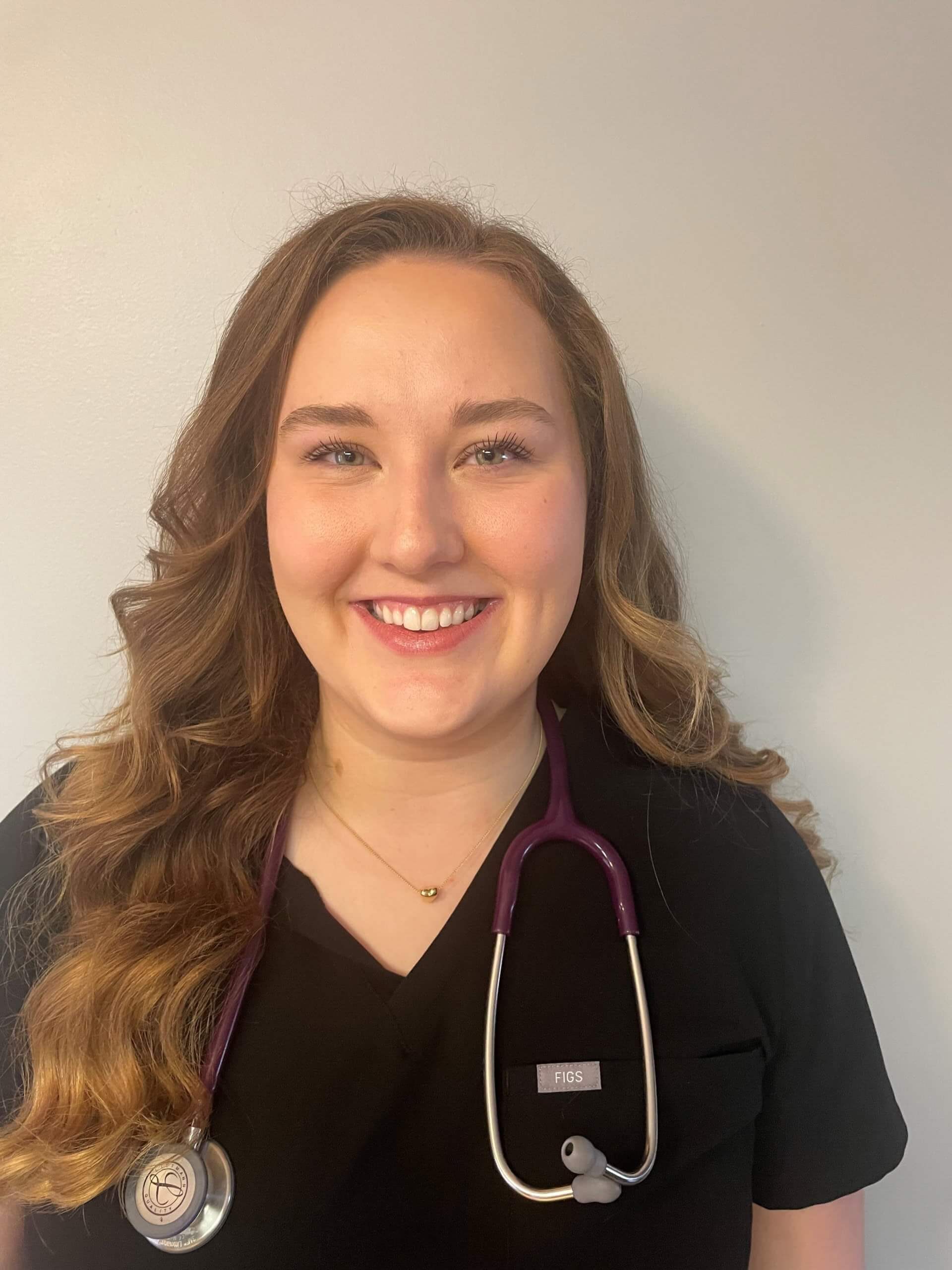 Smiling nurse in black scrubs with stethoscope around neck